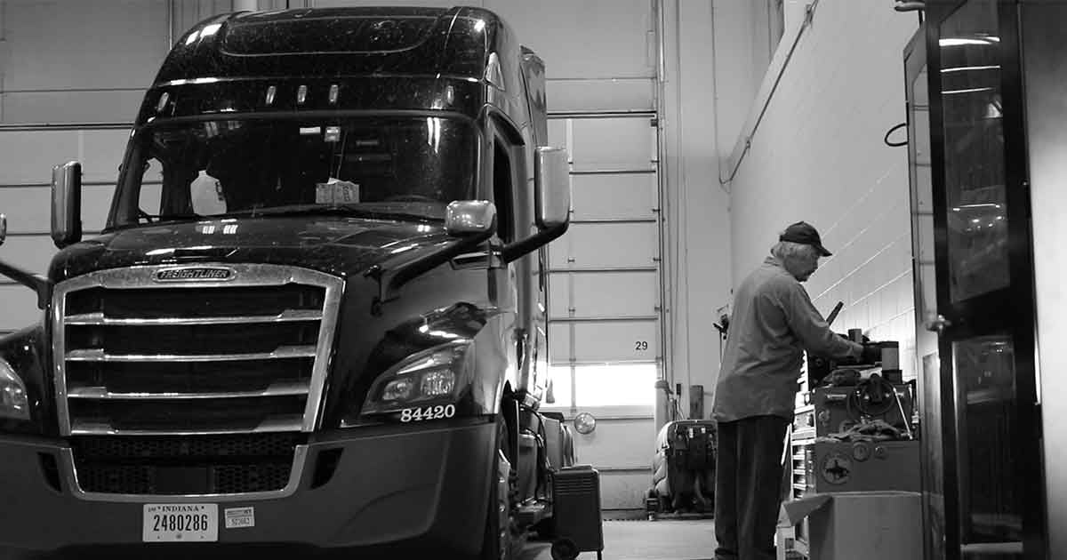 Mechanic checking tool box next to black semi truck