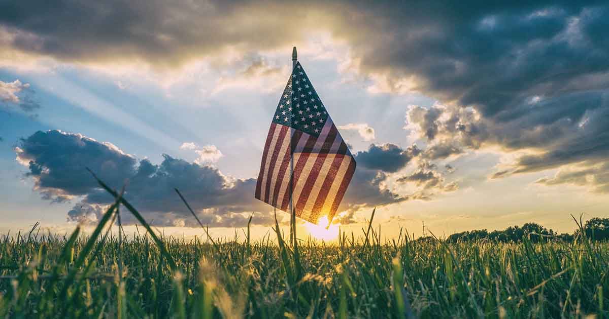 A miniature American flag in a corn field at sunset