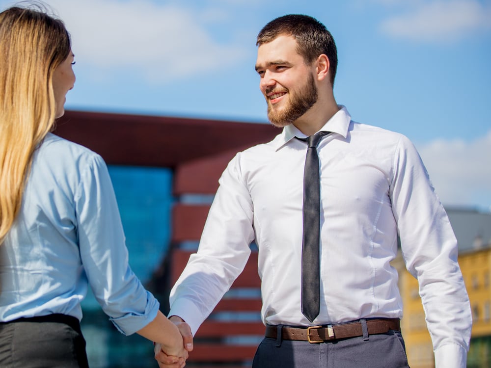 A man and a woman shake hands outdoors