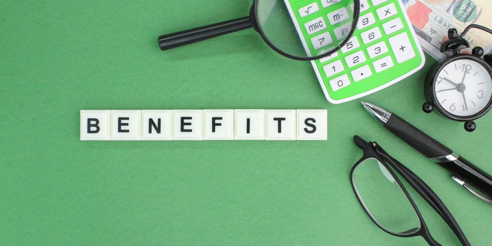 Benefits package concept with benefits written in all white, a pen, glasses, clock, calculator, and magnifying glass on a green background.