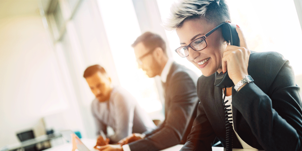 Businesswoman on the phone. Two men sit at the table near her.
