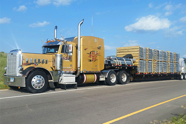 A gold-colored semi truck hauls a large flatbed load.